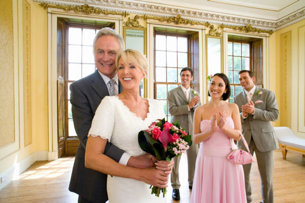 Mature couple posing for the camera with their adult children in the background, celebrating their wedding day