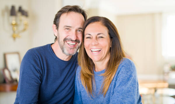 Middle-aged couple sitting together at home, smiling at the camera