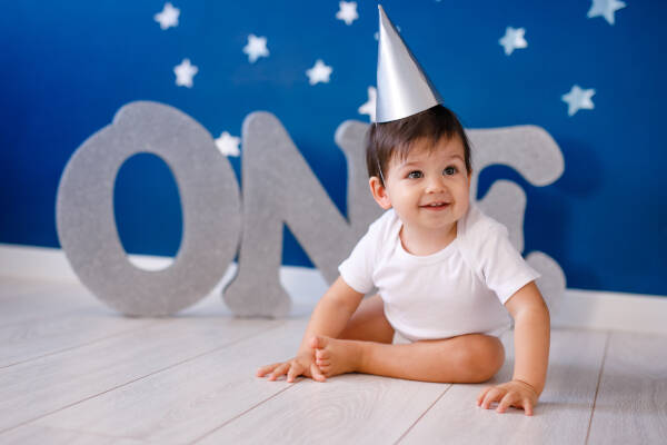 One-year-old boy celebrates birthday next to silver 'ONE' letters on blue background with stars