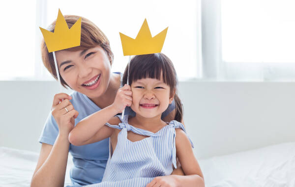 Portrait of mother and daughter playing and having fun together. They wear crowns on sticks