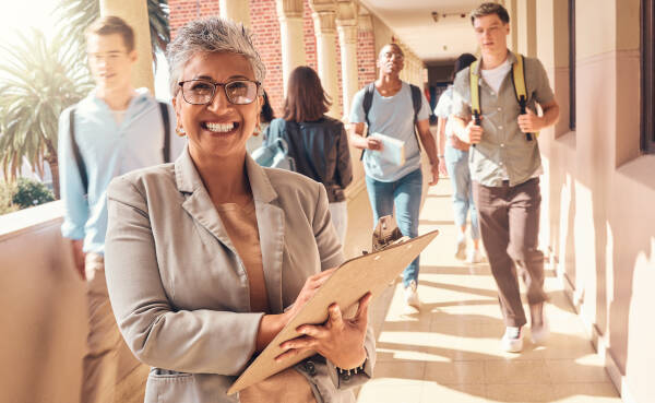 Principal stands and poses for a photo as teenage students walk by in the background
