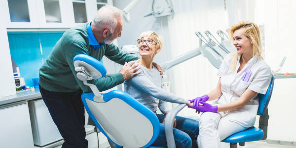 Senior couple and daughter dentist share smiles at the dentist's office, with the mother holding her daughter's hand