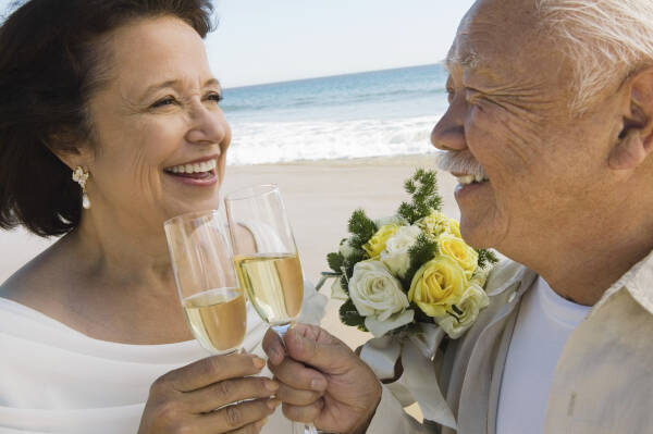 Senior newlyweds sharing a toast on the beach, smiling