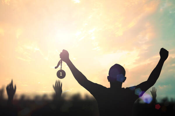 Silhouette of a champion's hand proudly holding a gold medal against a blurred autumn background
