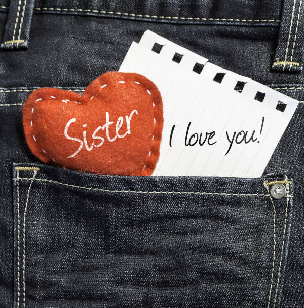 Sister, I love you! written on a piece of paper with a heart, against a jeans background.