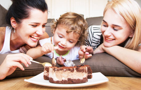 Sisters lays on the sofa with thier niece, all digging into a chocolate cake on the table.