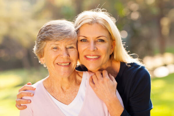 Smiling senior woman and middle-aged niece outdoors in a close-up portrait.