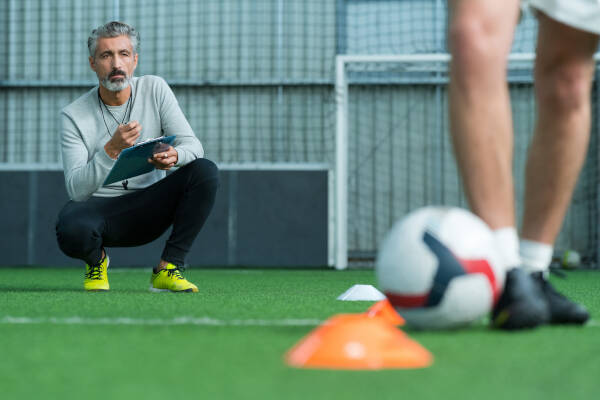 Soccer coach crouches down, offering guidance and training to a dedicated soccer player