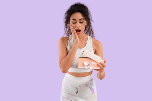 Sportswoman looks surprised as she opens a gift box against a lilac background