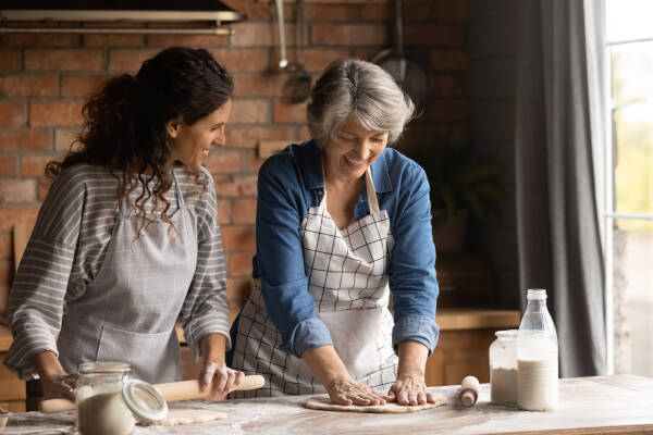 The adult niece and her auntie share a joyous moment as they cook together, rolling dough and sharing laughter.