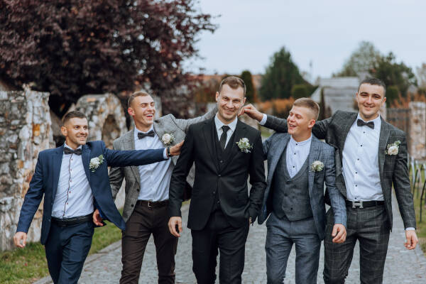 The groom and his friends pose in the yard, mingling in suits, goofing around, and smiling