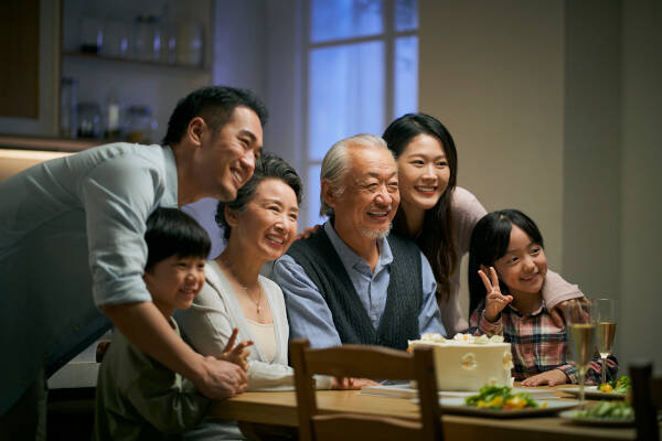 Three-generation family sitting at the dinner table, posing for the camera and smiling