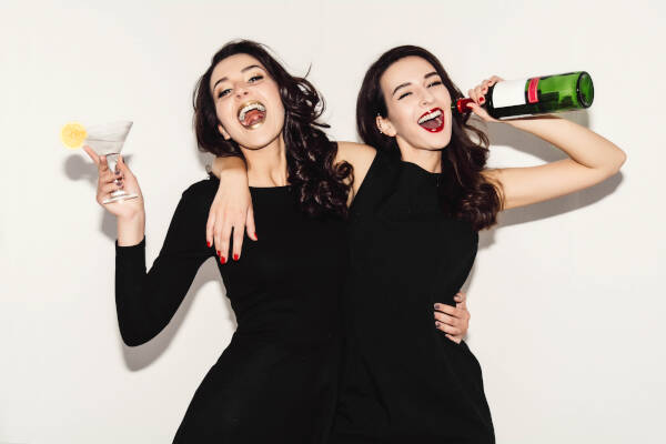 Two sisters in black night fashion dresses posing, isolated on a white-gray background.