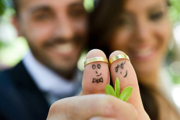 Wedding rings on fingers painted with funny little bride and groom figures