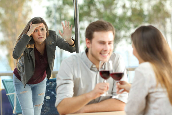 Woman looks through the window at her ex on a date in a coffee shop, contemplating emotions