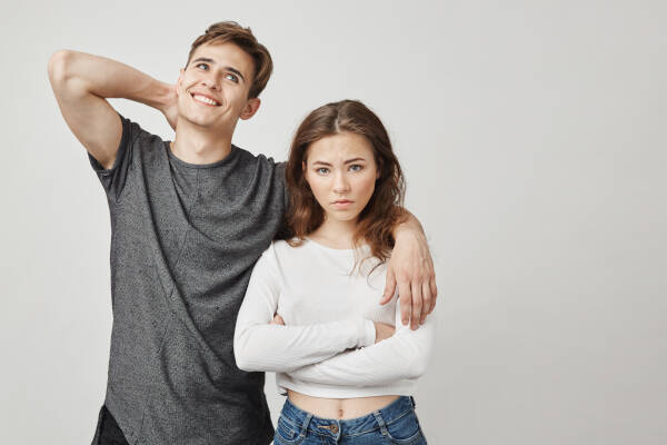 Woman stares into camera with a disappointed look as ex-boyfriend holds arm around her, looking up awkwardly