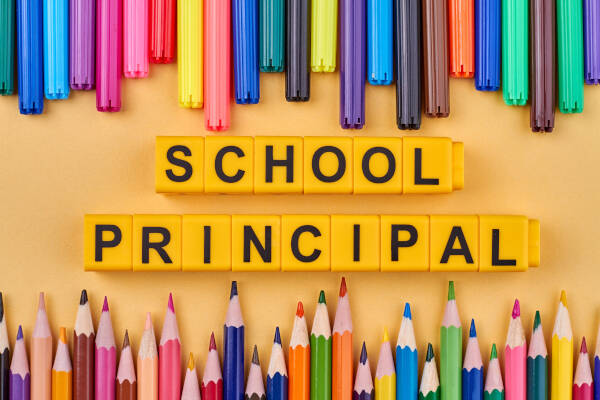 Yellow cubes spell out 'School Principal' amidst colorful pencils and felt pens on a vibrant background