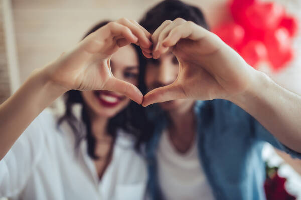 Young couple at home makes a heart sign with hands, smiling and looking at the camera
