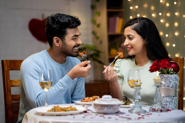 Young couple enjoys candlelit dinner at home, happily conversing over a meal