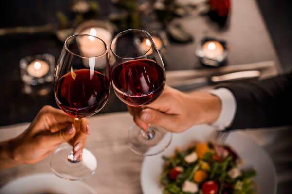 Young couple in close-up toast with glasses of red wine at a restaurant.