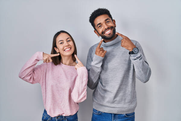 Young couple stands together, smiling cheerfully, pointing to their teeth and mouths