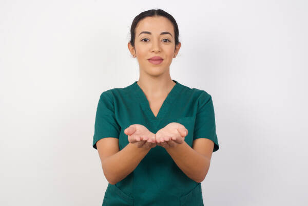 Young dentist woman holds out open palms against an isolated white background