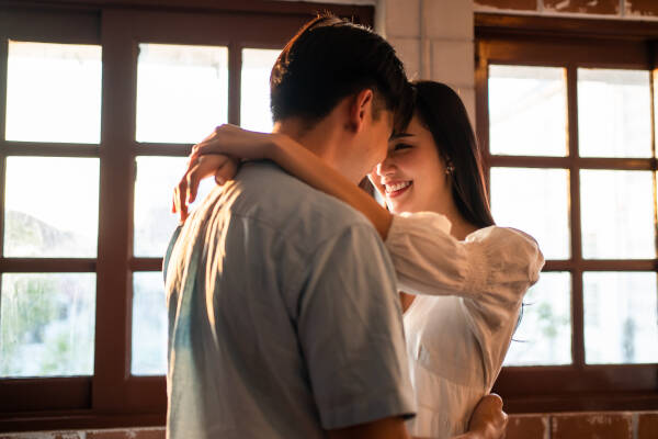 Young man and woman embrace in the living room at home, man facing away from the camera and the woman smiling.