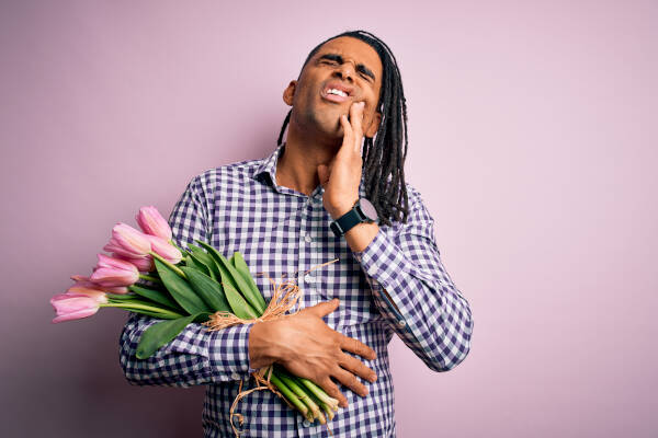 Young man holds bouquet of pink tulips, touching mouth with painful expression due to toothache