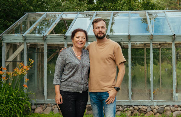 Young man smiles with aunt outside in front of a glass greenhouse