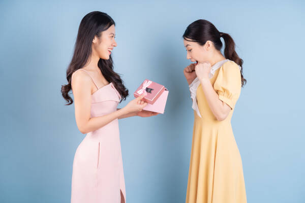 Young woman holding a pink gift box to give to her sister, against a blue background