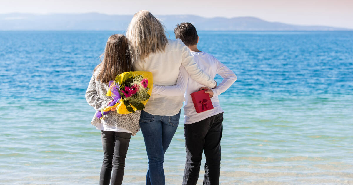 Mother and her two kids cherish the beach view. Kids prepare gifts. Theme is celebrating and appreciating mom.