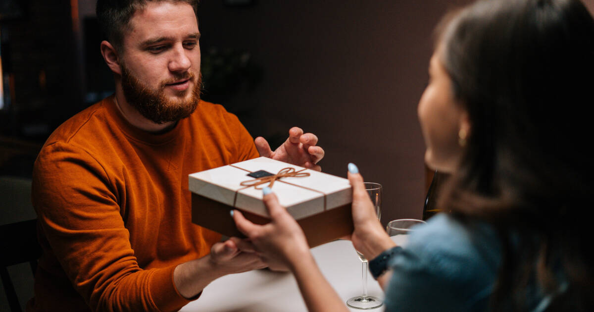 Happy young man receives a present from his loving girlfriend as they enjoy dinner together.