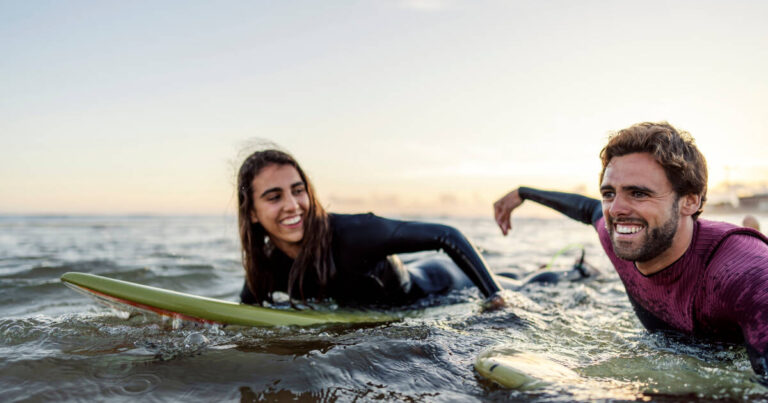Surfers lying on their bellies on surfboards in the sea, smiling.