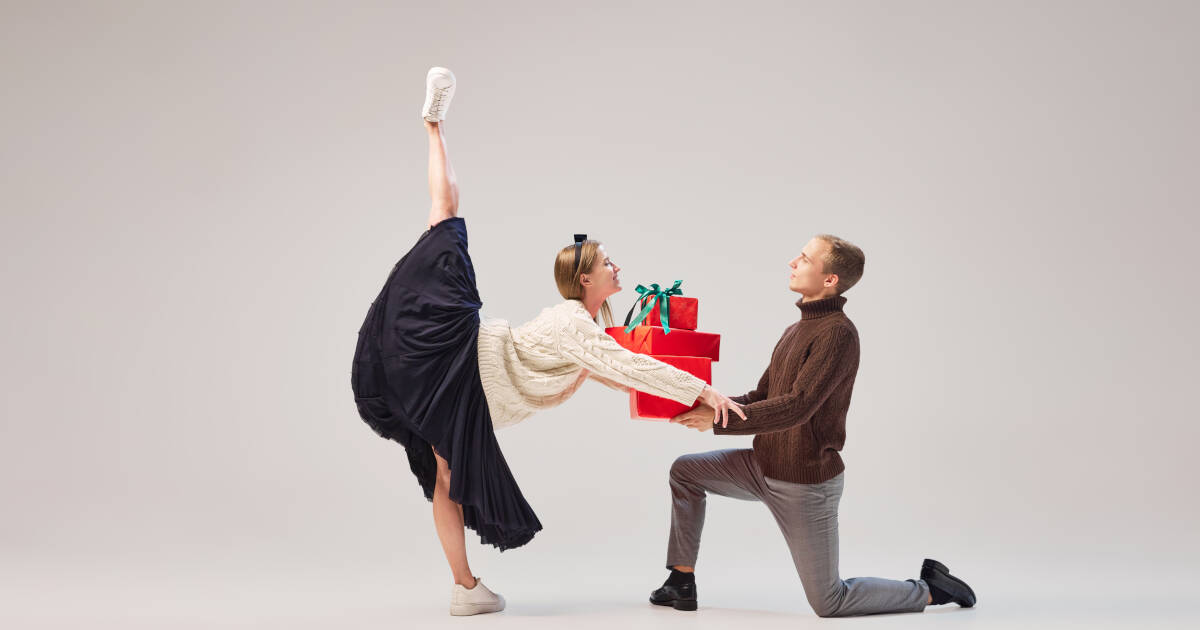 A portrait of a man, and a woman dancer, in elegant motion. The male passes gift boxes to the woman on a gray background.