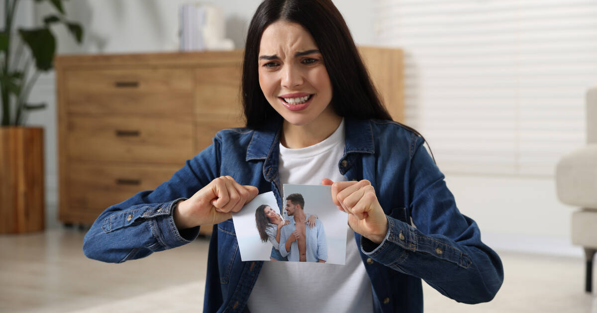 Upset woman at home, tearing apart a photo, symbolizing the concept of breakup