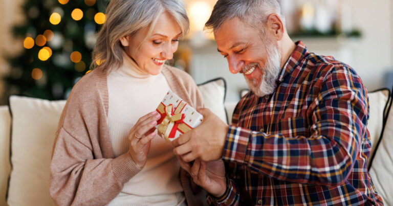 Mature couple exchanging Christmas presents sitting on sofa at home.