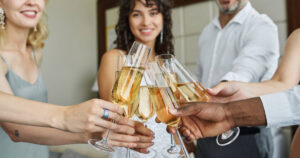 Guests clinking champagne flutes in front of the camera, standing in a circle at the engagement party.