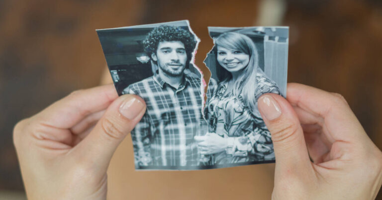 A hand tearing a photo of a male and female couple.