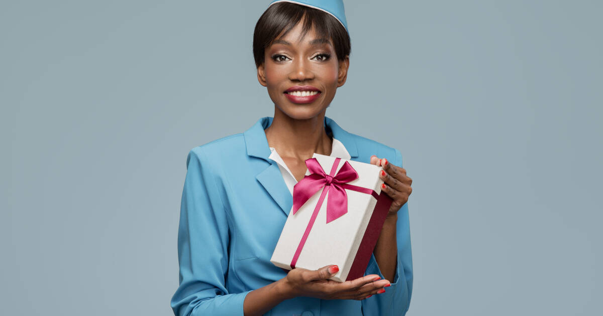 Smiling young stewardess holding a gift box against a blue background.