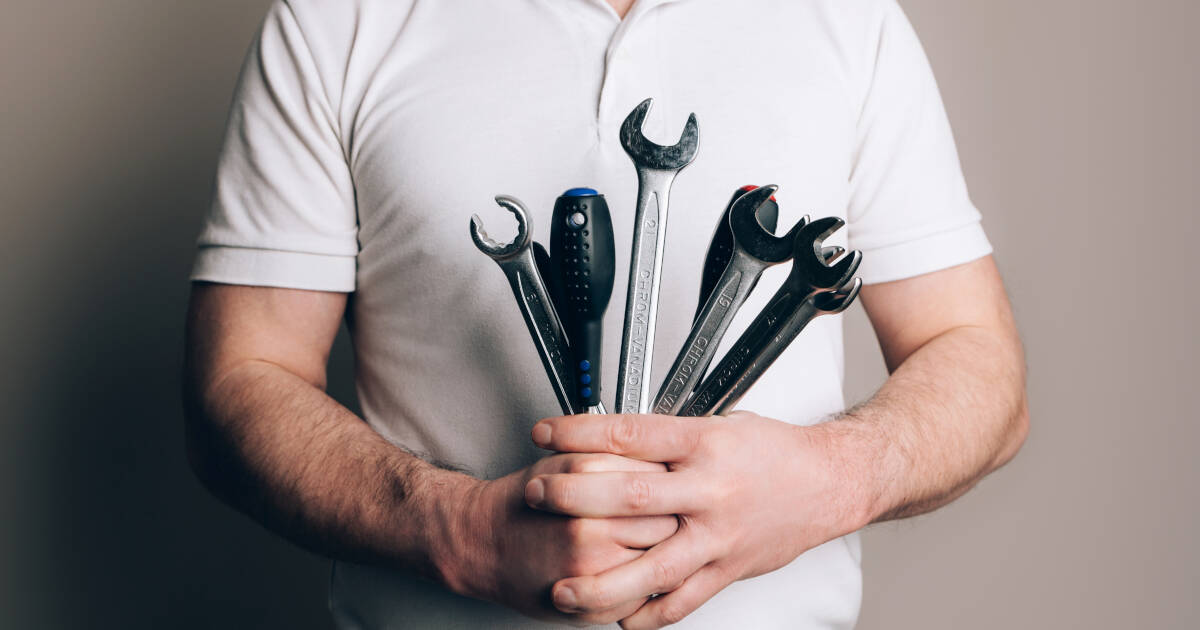 Close up of a man's hands holding a set of tools, including wrenches, screwdrivers.