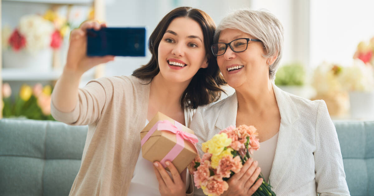 Beautiful young woman and her mother at home with flowers and a gift box, celebrating Mother's Day