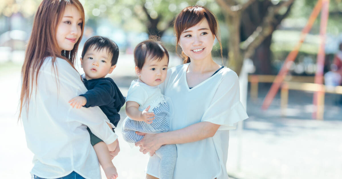 Two women smiling at the camera while holding their young children in their arms.