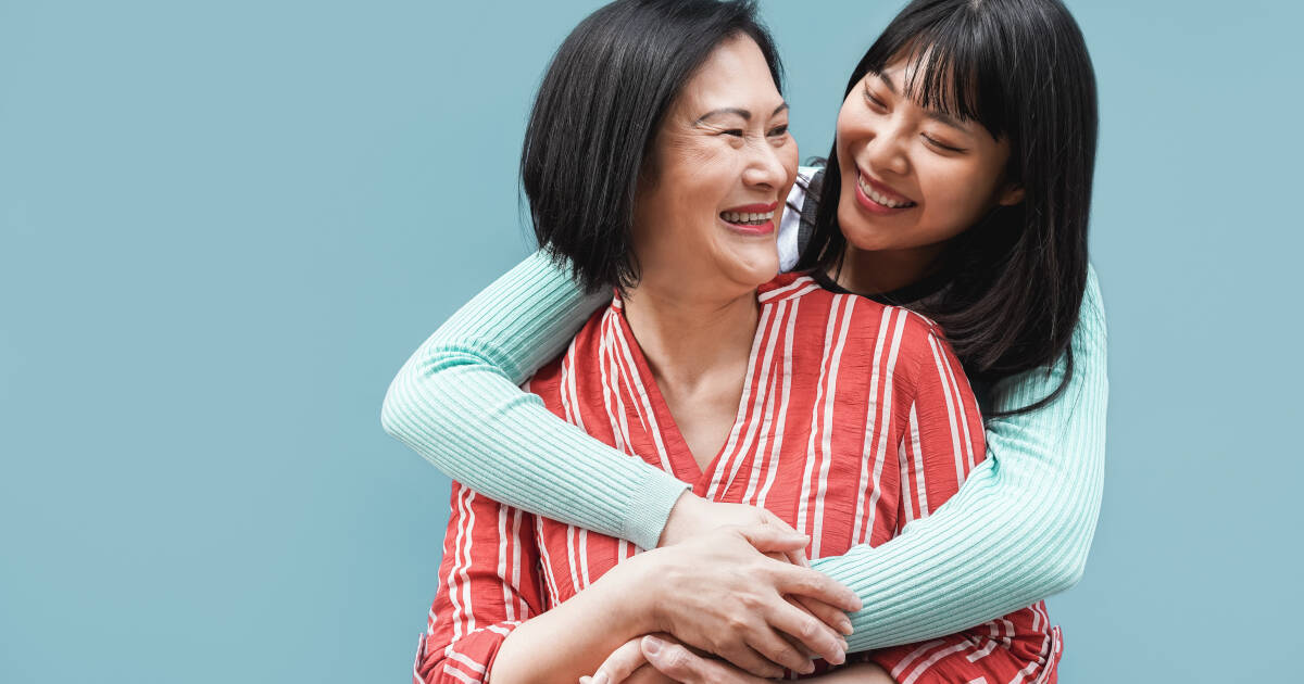 auntie and niece share a warm embrace, their smiles radiating against a light blue backdrop