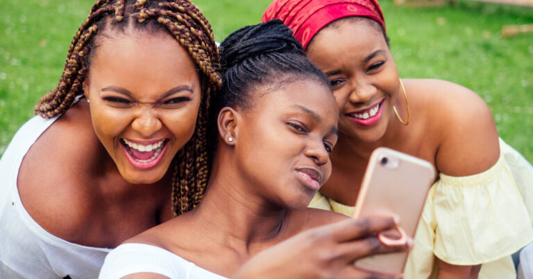 Three sisters sit outdoors and pose for a selfie together, all wearing bright smiles