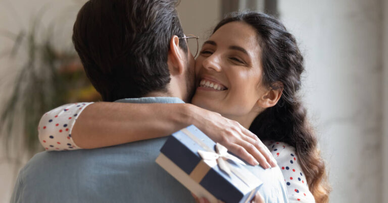 Close up of an overjoyed wife hugging her husband holding a gift box in her hand.