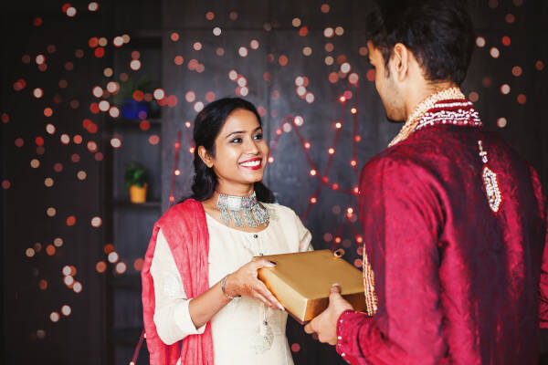 Woman smiles widely as she gives gift box to husband