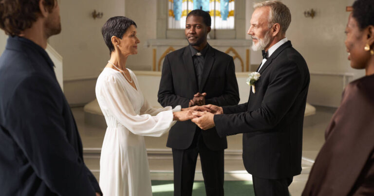 Senior couple as bride and groom hold hands at church altar on wedding day, with friends and family watching.