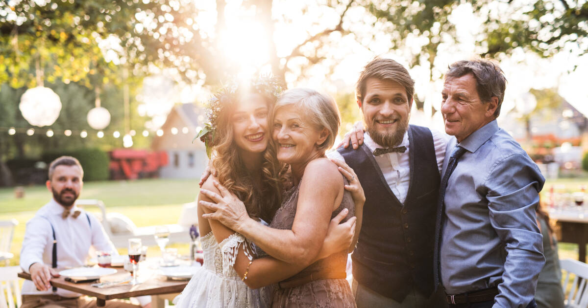 Bride, groom, and parents posing for a photo at wedding reception outside in the backyard.