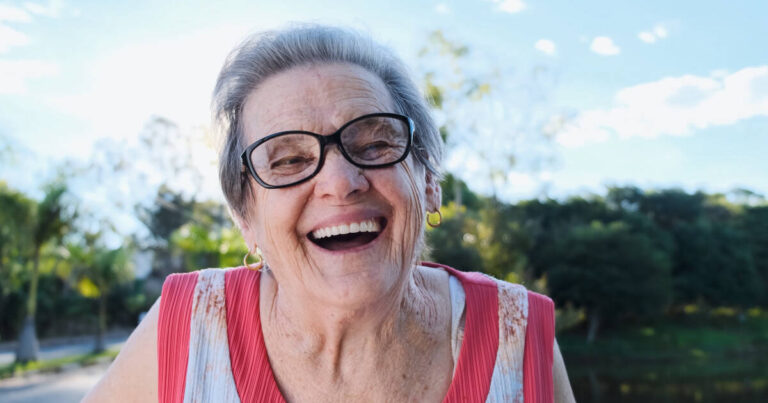 Close-up shot of a 75-year-old woman laughing outside.