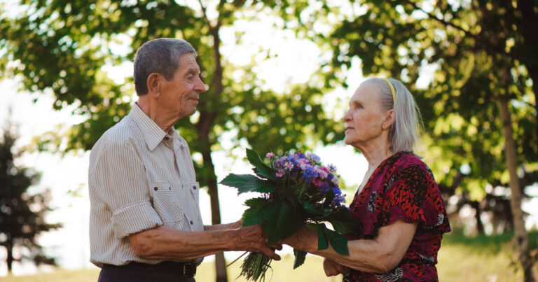 An Elderly Man Gives colorful Flowers To an elderly woman of 80 years old.